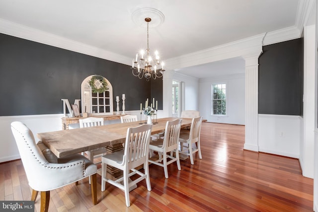 dining room with hardwood / wood-style floors, decorative columns, ornamental molding, and a notable chandelier