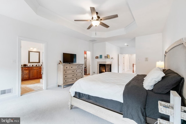 bedroom featuring ensuite bathroom, ornamental molding, a tray ceiling, light colored carpet, and ceiling fan