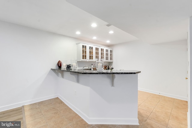 kitchen featuring white cabinets, a breakfast bar, kitchen peninsula, and light tile patterned floors