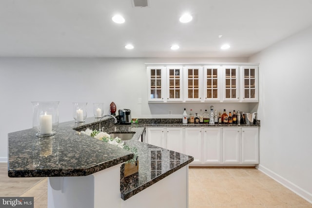 kitchen featuring white cabinetry, dark stone countertops, kitchen peninsula, and sink