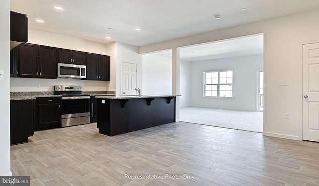 kitchen with a kitchen island with sink, a kitchen breakfast bar, sink, light stone countertops, and appliances with stainless steel finishes