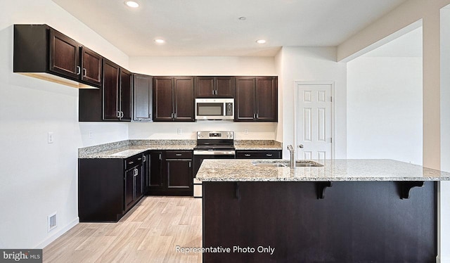 kitchen featuring a breakfast bar, sink, light wood-type flooring, appliances with stainless steel finishes, and light stone counters