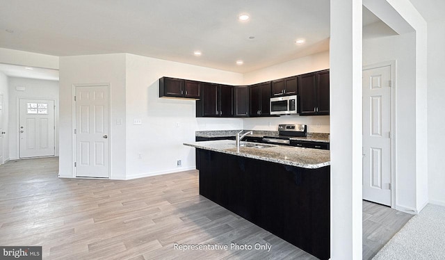 kitchen featuring sink, light wood-type flooring, dark brown cabinets, light stone counters, and stainless steel appliances