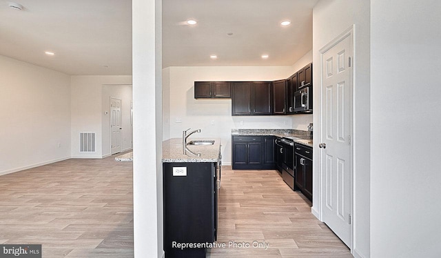 kitchen with appliances with stainless steel finishes, light wood-type flooring, light stone counters, and sink