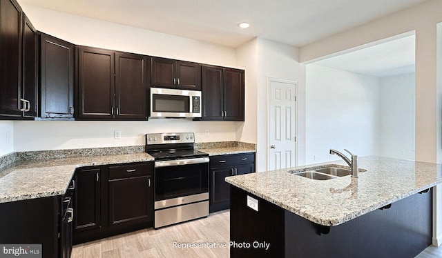 kitchen featuring sink, light stone countertops, appliances with stainless steel finishes, light hardwood / wood-style floors, and a kitchen bar