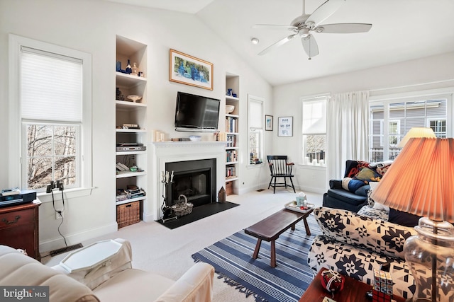 carpeted living room with built in shelves, a wealth of natural light, lofted ceiling, and ceiling fan