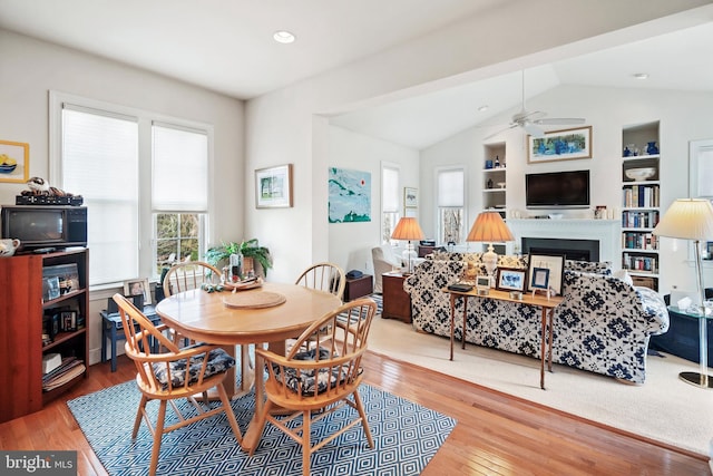 dining space with built in shelves, ceiling fan, wood-type flooring, and vaulted ceiling