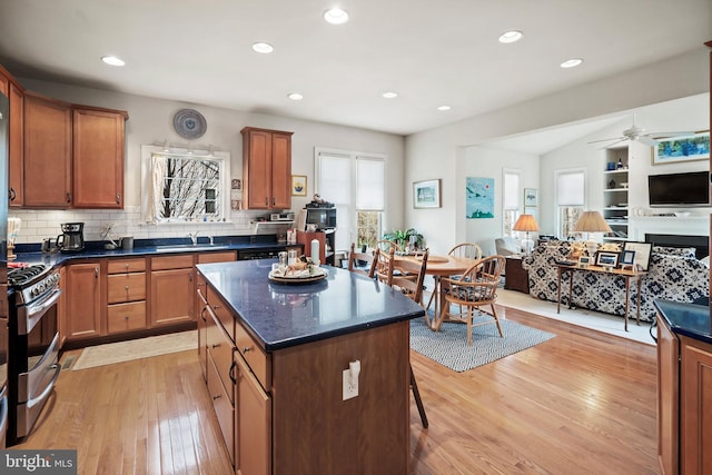 kitchen featuring sink, stainless steel gas range, ceiling fan, decorative backsplash, and light hardwood / wood-style floors