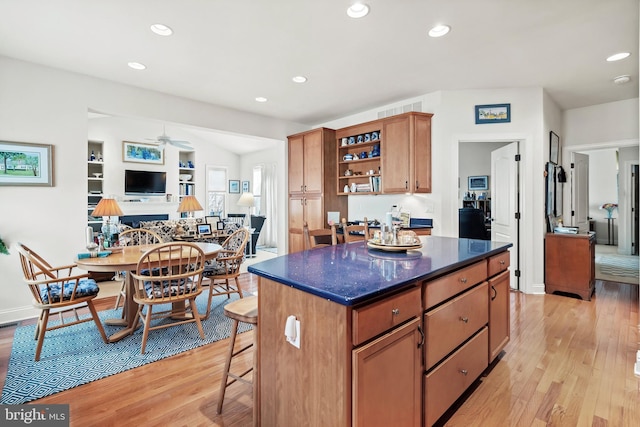 kitchen with light hardwood / wood-style floors, a kitchen island, ceiling fan, and a breakfast bar area