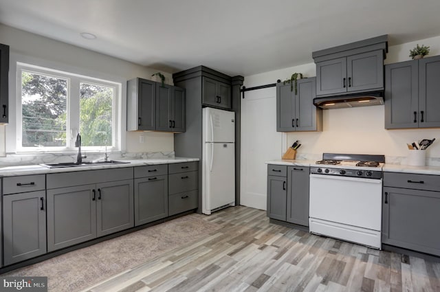 kitchen featuring gray cabinetry, white appliances, sink, a barn door, and light hardwood / wood-style floors