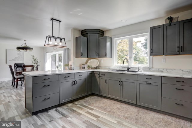 kitchen with light stone countertops, sink, pendant lighting, light hardwood / wood-style floors, and gray cabinets