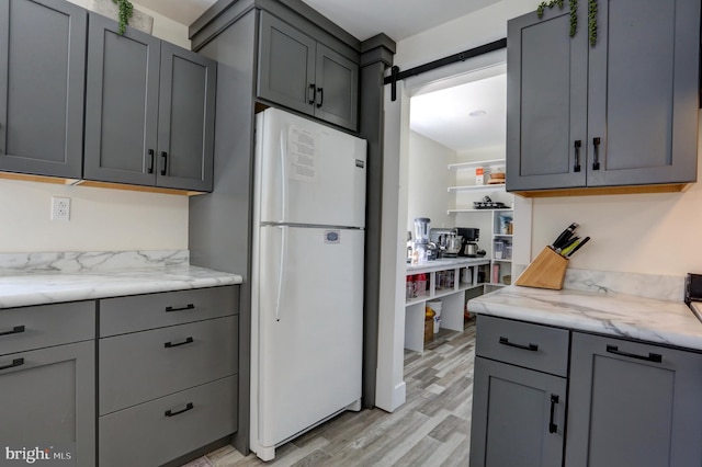 kitchen featuring light hardwood / wood-style flooring, gray cabinets, a barn door, white fridge, and light stone counters