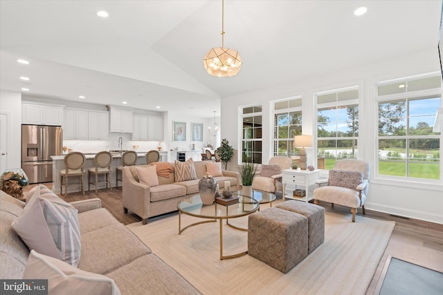 living room with a chandelier, light wood-type flooring, lofted ceiling, and sink