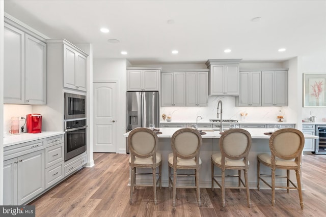 kitchen featuring beverage cooler, stainless steel appliances, an island with sink, a kitchen bar, and hardwood / wood-style flooring