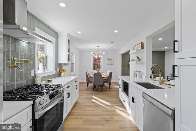 kitchen with sink, wall chimney range hood, appliances with stainless steel finishes, white cabinets, and light wood-type flooring