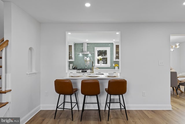 bar with stainless steel range, light hardwood / wood-style floors, white cabinets, and wall chimney range hood