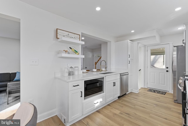 kitchen with sink, stainless steel dishwasher, light hardwood / wood-style floors, white cabinetry, and black microwave