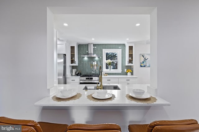 bar featuring decorative backsplash, stainless steel appliances, white cabinetry, and wall chimney range hood