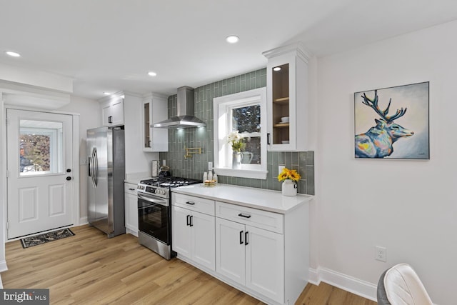 kitchen featuring appliances with stainless steel finishes, light wood-type flooring, tasteful backsplash, wall chimney range hood, and white cabinets