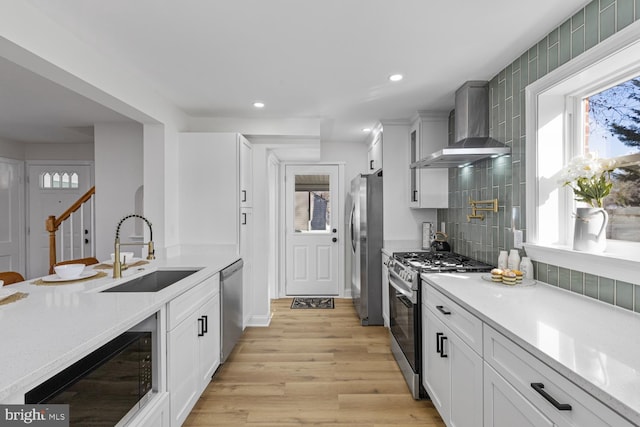 kitchen featuring sink, stainless steel appliances, wall chimney range hood, light hardwood / wood-style floors, and decorative backsplash