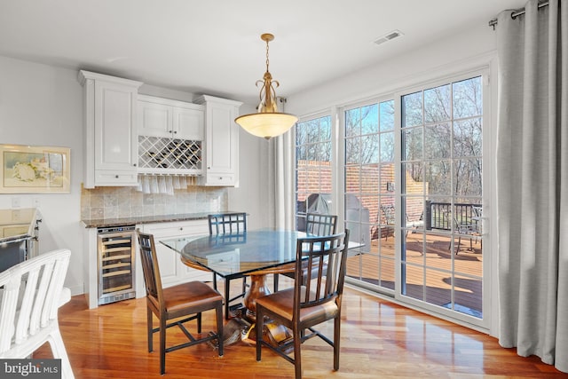 dining space featuring bar area, light hardwood / wood-style flooring, and beverage cooler