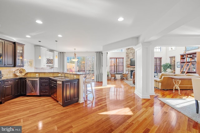 kitchen with decorative columns, stainless steel dishwasher, a breakfast bar, dark brown cabinets, and light hardwood / wood-style floors