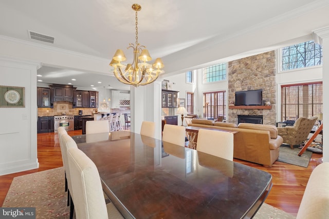 dining space with light hardwood / wood-style floors, a stone fireplace, ornamental molding, and an inviting chandelier