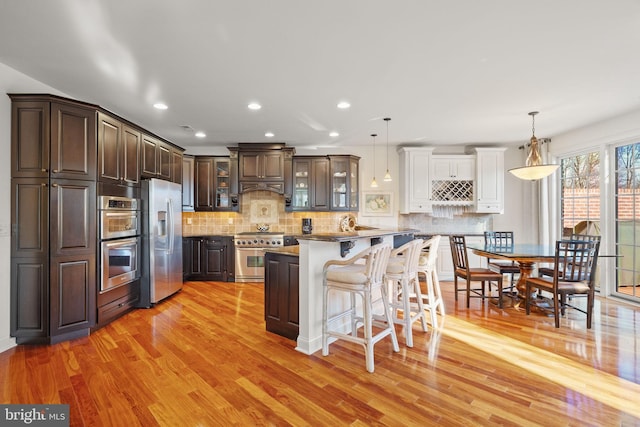 kitchen with pendant lighting, a kitchen breakfast bar, stainless steel appliances, and light hardwood / wood-style flooring