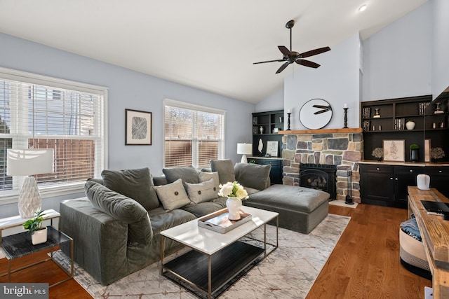 living room featuring a fireplace, light wood-type flooring, ceiling fan, and vaulted ceiling