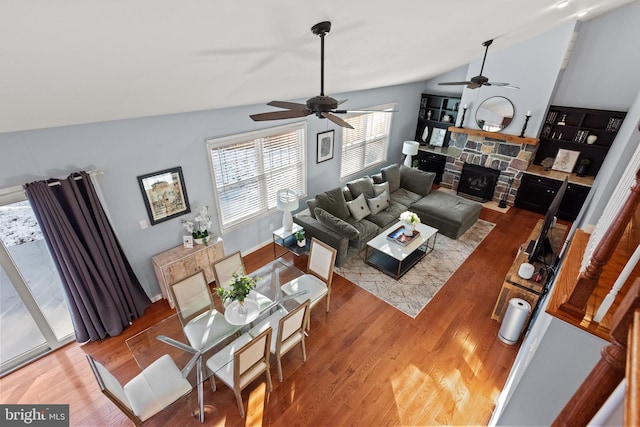 living room featuring vaulted ceiling, ceiling fan, hardwood / wood-style flooring, and a stone fireplace