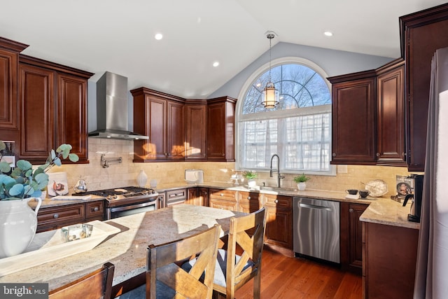 kitchen with stainless steel appliances, vaulted ceiling, light stone counters, wall chimney range hood, and pendant lighting