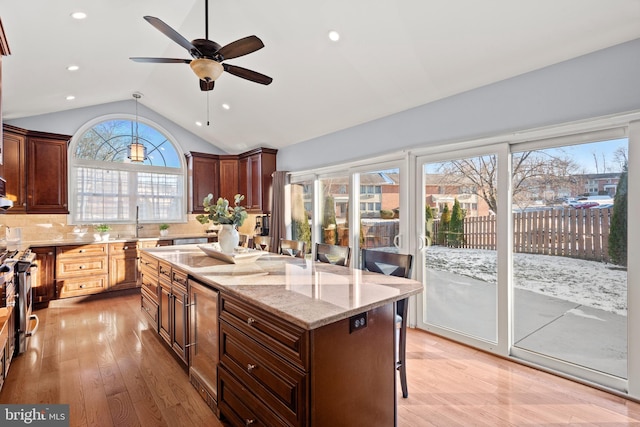 kitchen featuring vaulted ceiling, ceiling fan, tasteful backsplash, light hardwood / wood-style floors, and a breakfast bar