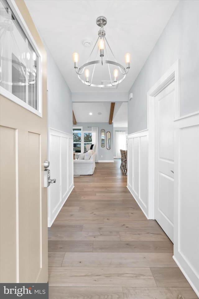 hall with beamed ceiling, light hardwood / wood-style flooring, and an inviting chandelier