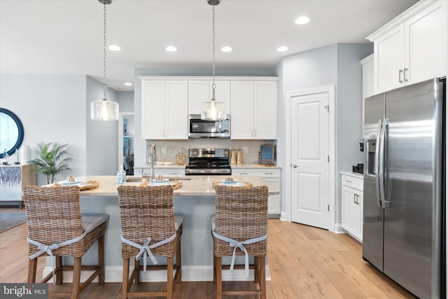 kitchen featuring stainless steel appliances, sink, light hardwood / wood-style flooring, white cabinets, and hanging light fixtures