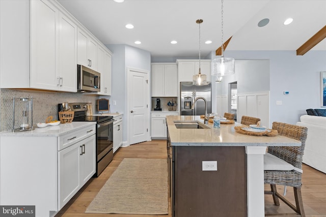 kitchen featuring a center island with sink, hanging light fixtures, light wood-type flooring, appliances with stainless steel finishes, and white cabinetry