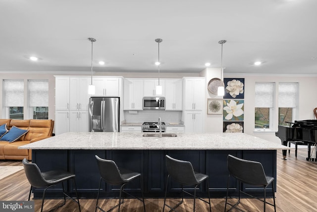 kitchen with stainless steel appliances, pendant lighting, a large island with sink, hardwood / wood-style flooring, and white cabinets