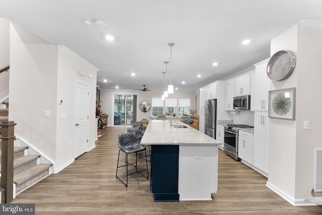 kitchen featuring appliances with stainless steel finishes, white cabinetry, a kitchen island with sink, and ceiling fan