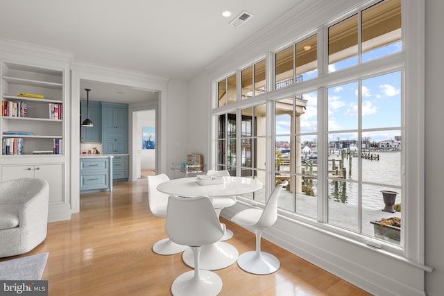 dining space with crown molding, a water view, and light hardwood / wood-style floors