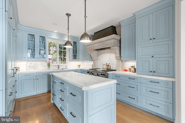 kitchen featuring sink, hanging light fixtures, light wood-type flooring, a kitchen island, and stove