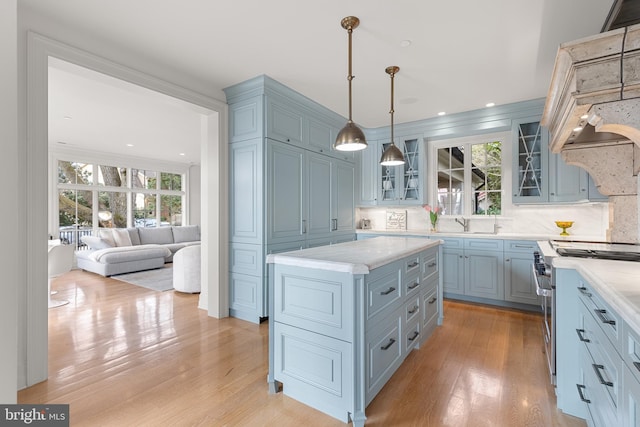 kitchen featuring a kitchen island, backsplash, high end range, hanging light fixtures, and light hardwood / wood-style flooring