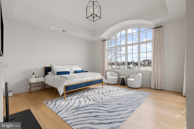 bedroom with a tray ceiling, a notable chandelier, and light hardwood / wood-style flooring