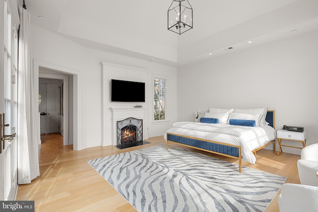 bedroom with a tray ceiling, a chandelier, and light hardwood / wood-style flooring