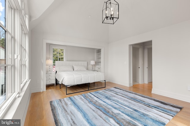 bedroom featuring an inviting chandelier, light hardwood / wood-style flooring, and high vaulted ceiling