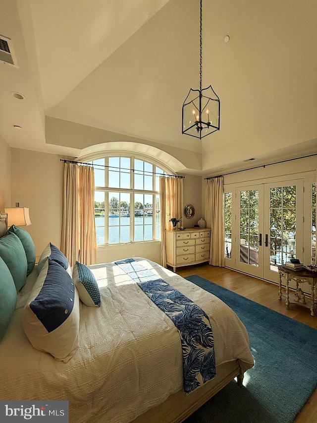 bedroom with hardwood / wood-style flooring, access to outside, a tray ceiling, a water view, and french doors