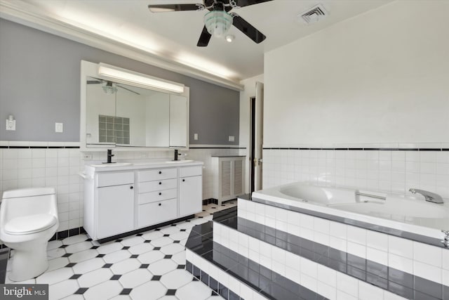 bathroom with vanity, ceiling fan, a relaxing tiled tub, tile walls, and toilet