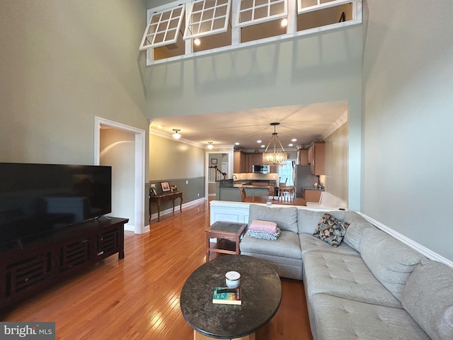 living room with a notable chandelier, light wood-type flooring, crown molding, and a high ceiling