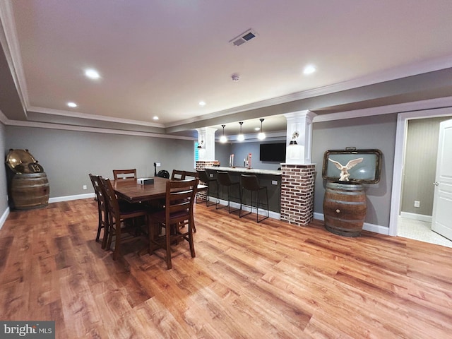 dining space with bar area, crown molding, and light wood-type flooring