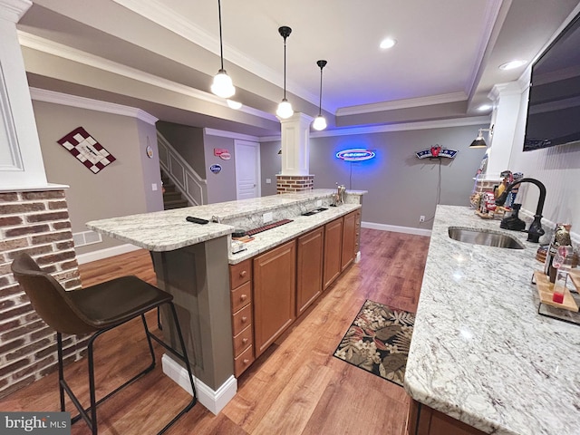 kitchen featuring light stone countertops, sink, crown molding, light hardwood / wood-style floors, and a kitchen bar