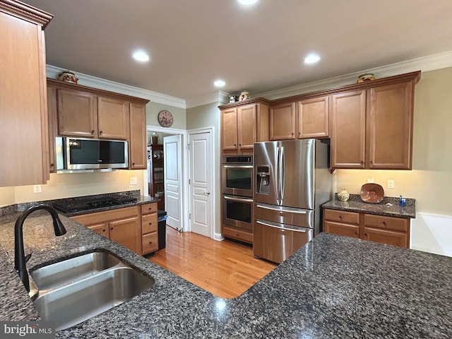 kitchen with sink, crown molding, dark stone counters, appliances with stainless steel finishes, and light wood-type flooring