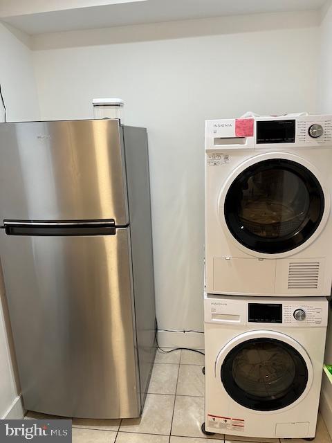 laundry area with stacked washing maching and dryer and light tile patterned floors